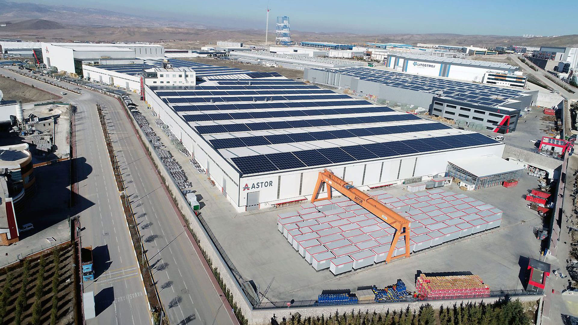 Astor Enerji üretim tesisinin güneş panelleriyle kaplı çatıları, fabrika binaları ve açık depolama sahasının havadan görünümü.