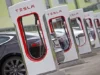 Sıra halinde beyaz ve kırmızı Tesla Supercharger üniteleri ve park edilmiş araçlar; arşiv görseli