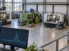 Yük faktörü nedir? 100 kW ve yüzde 50 hesaplama örneği Sanayi atölyesindeki elektrikli üretim makineleri ve ön planda kısa süreli güç zirvesi gösteren etiketsiz tüketim eğrisinin bulunduğu enerji izleme ekranı